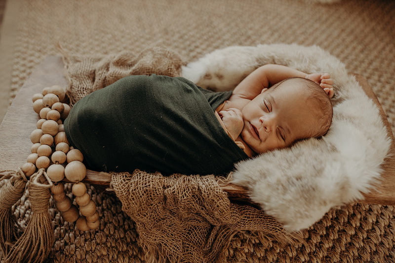 Newborn Photography, a baby seemingly smiling lays cozily wrapped in blankets on a wooden cradle
