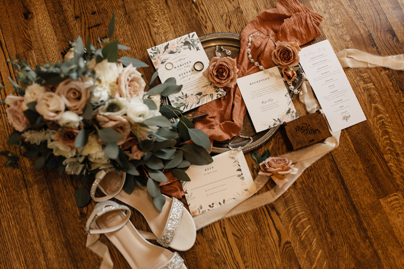 Photography Studio on Main, on a wooden floor sits various bridal outfit accessories, cards, flowers, and decorations.