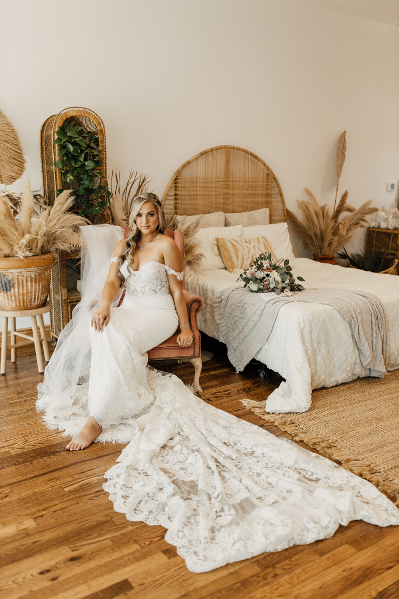 Photography Studio on Main, a woman sits on a chair in a boho style room with white dress and long train draped out on floor