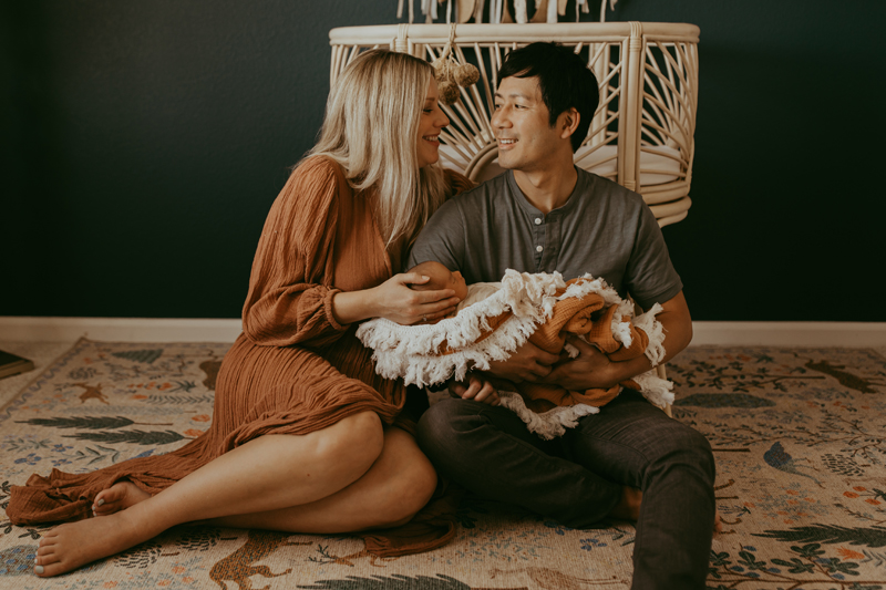 Newborn Photography, a man and woman sit beside each other on a rug, dad holds baby