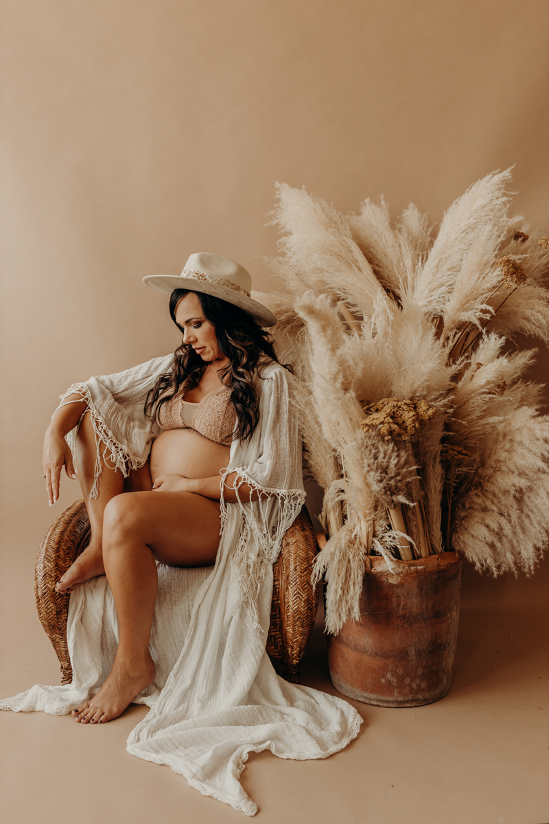 Maternity Photography, a woman sits in a boho style room with pampas grass behind her