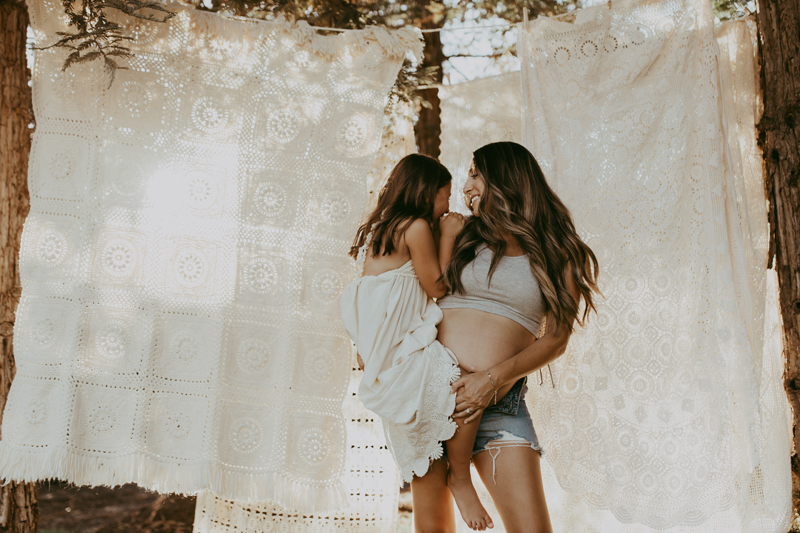 Maternity Photography, a pregnant woman holds her daughter before a clothesline with hanging sheets oustide
