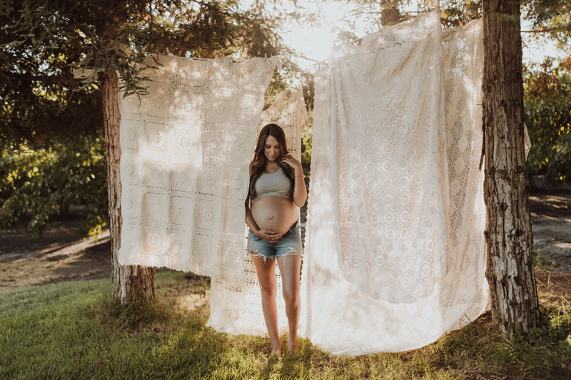 Maternity Photography, a pregnant mother stands outdoors before a clothesline with hanging linens.