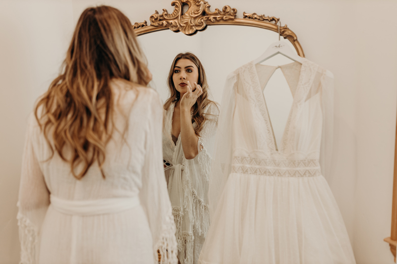 Photography Studio on Main, a woman examines herself before a mirror, she is in a white dress