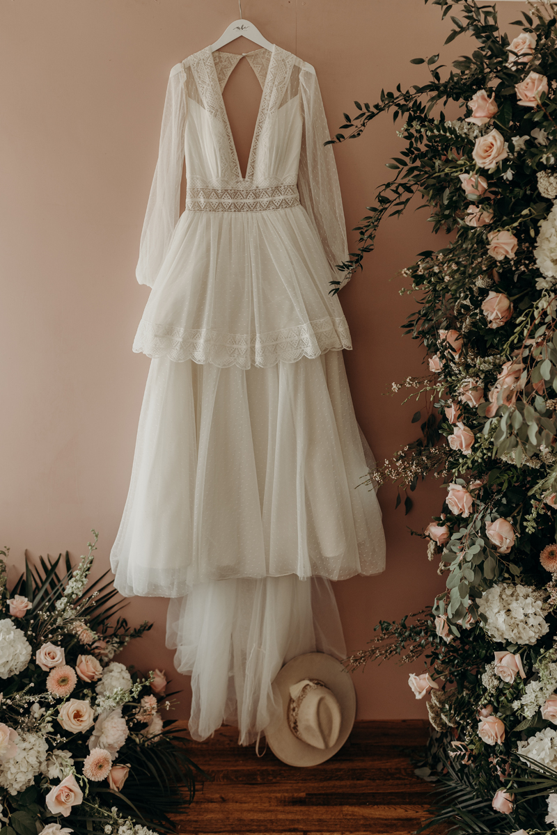 Photography Studio on Main, a white dress hangs on a wall beside an arrangement of pastel roses