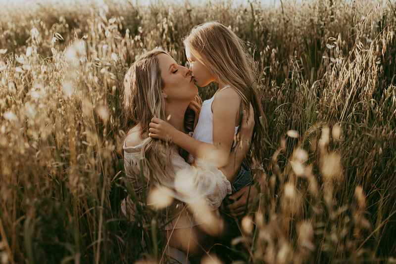 Maternity Photography, a woman kisses her daughter, she holds her little girl in tall dry grass