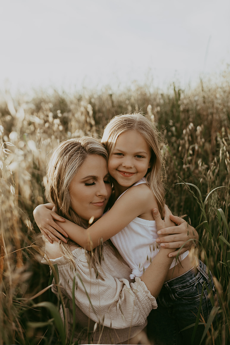 Maternity Photography, a mother holds her smiling young daughter, they stand in a field of tall dry grass