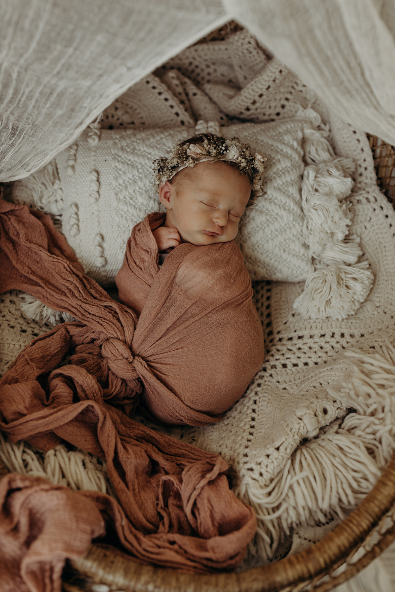 Newborn Photography, a baby sleeps happily swaddled in blankets within a wicker basket
