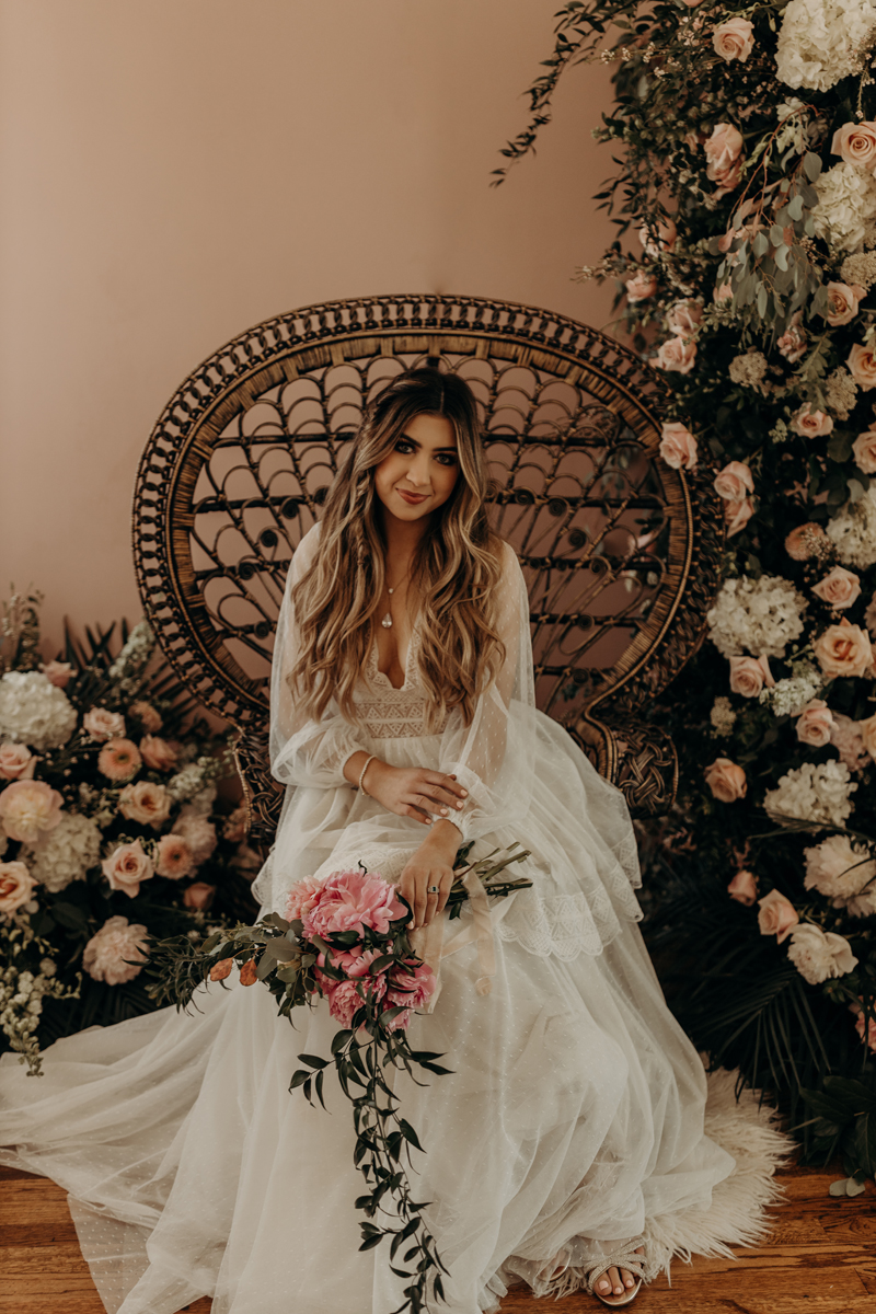 Photography Studio on Main, a young woman in a wedding dress holds a bouquet of roses in a large wicker chair with more roses surrounding it