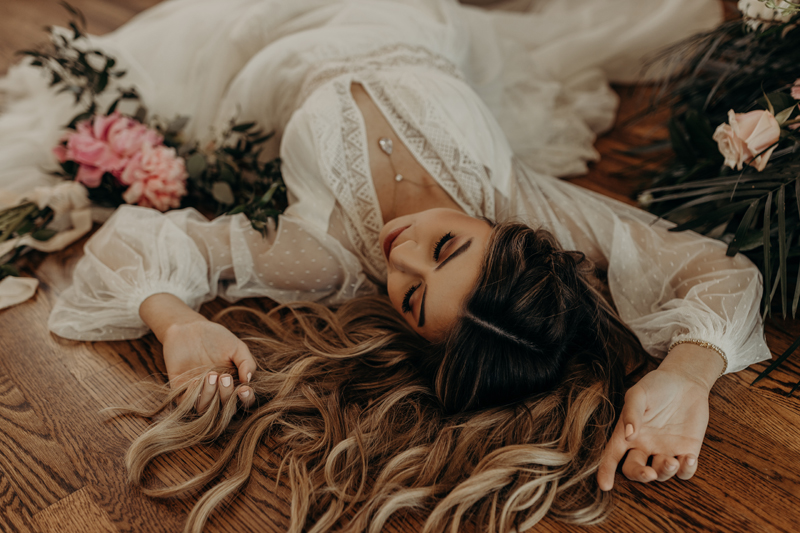 Photography Studio on Main, a woman in a white dress lays on the floor content, her spread on the ground and flowers surrounding her