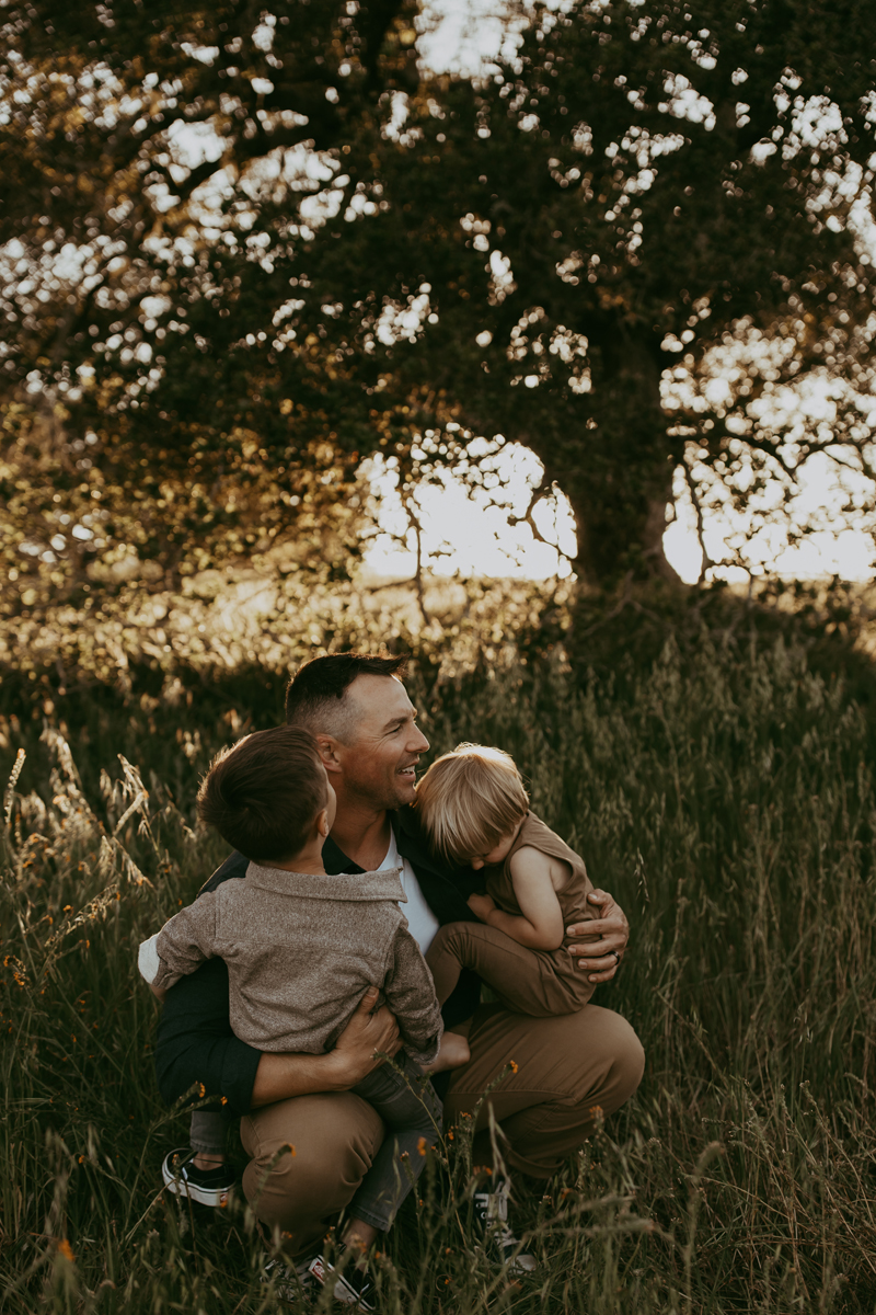 Family Photography, a dad holds his two young sons beneath a tree in the tall grass