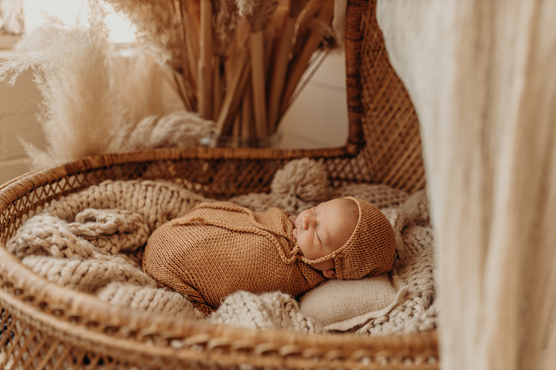 Newborn Photography, a baby is wrapped in blankets and lays sleeping a wicker cradle