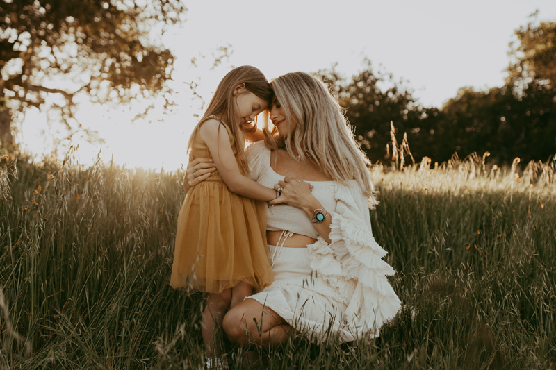 Family Photography, a mother and young daughter hold each other outside in the tall grass