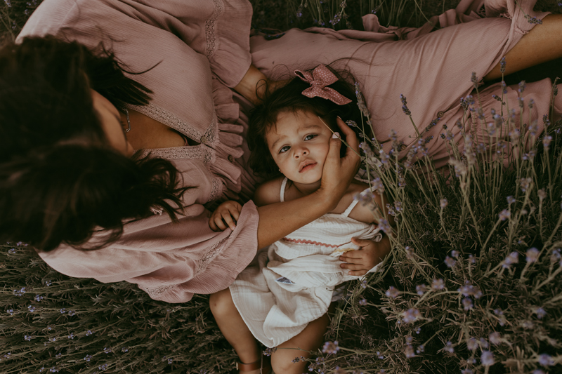 Family Photography, a young baby girl lays in her mothers lap outdoors with wild lavender growing beside them