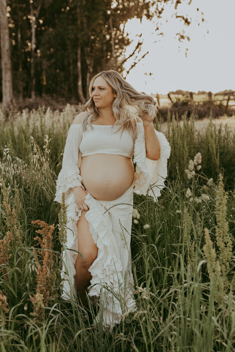 Maternity Photography, a woman walks through a tall grassy meadow, she is expecting and happy