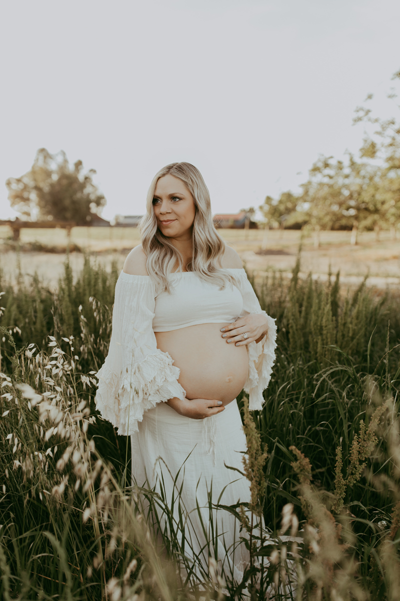 Maternity Photography, a woman holds her belly outdoors in a field she is expecting